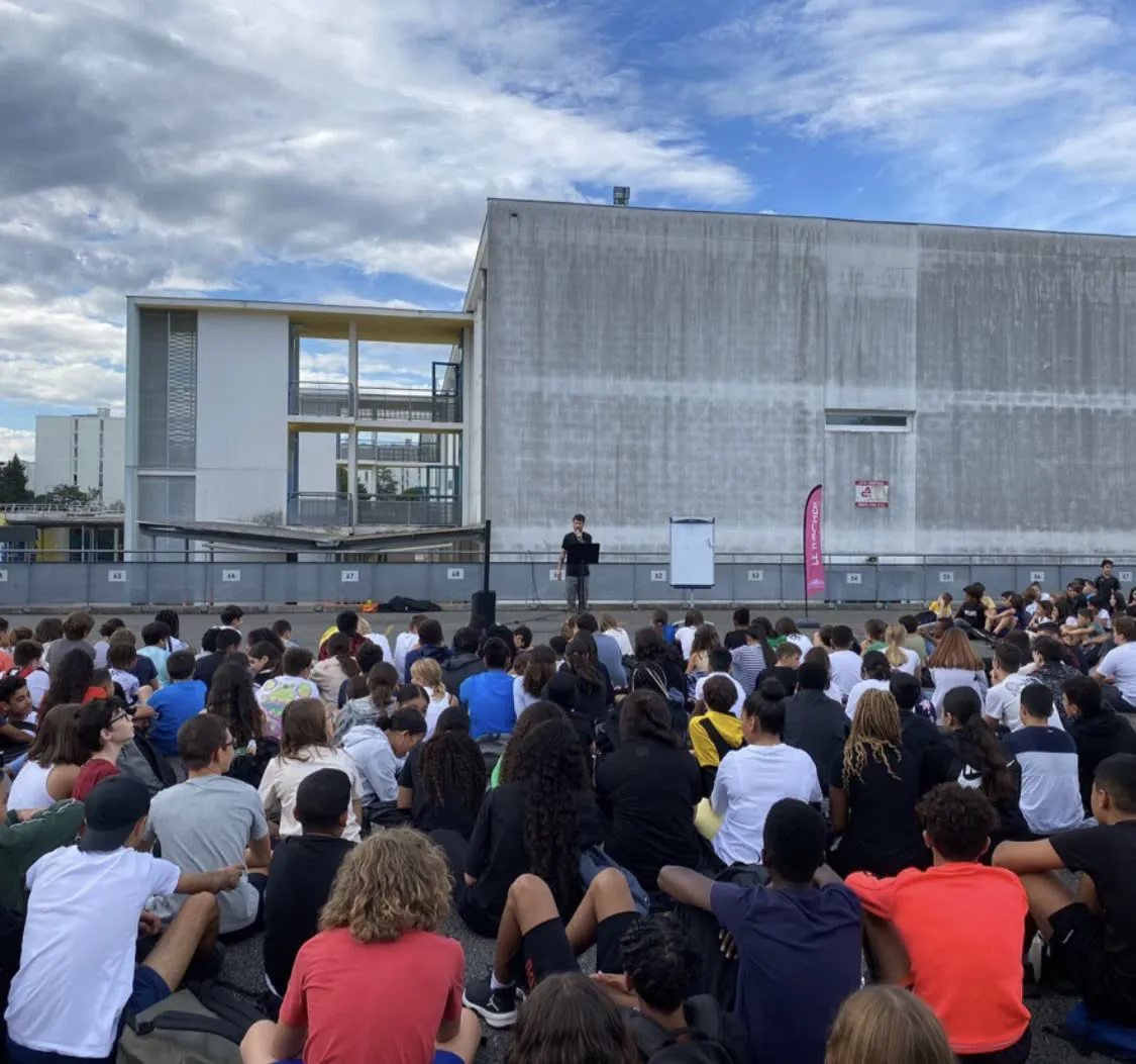 Un passage au micro devant des centaines d’élèves assis dans la cour de l’établissement